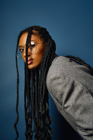 Young woman with long braids leans slightly, flaunting her stylish glasses and confidence.