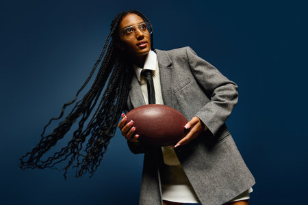 A young woman wears a tailored blazer and holds a football while showcasing her vibrant personality.の写真素材