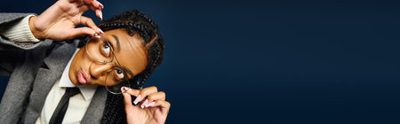 Bright eyed young woman with braided hair is playfully adjusting her glasses with a smile.の写真素材