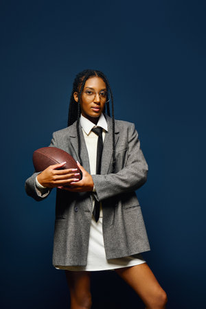 A confident young woman showcases her unique style while holding a football in her arms.の写真素材