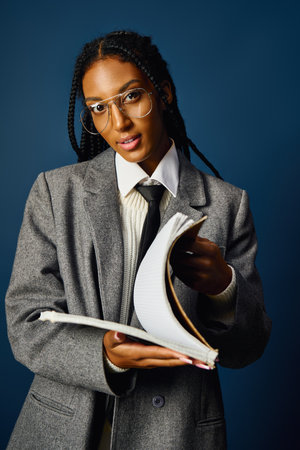 In a modern environment, a young woman shows off her stylish outfit while reading from a notebook.の写真素材