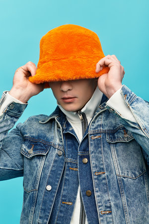 Sporting an eye catching orange hat, a young man showcases his trendy style while posing playfully.