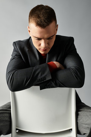 A handsome young man sits calmly on a chair, lost in thought, wearing a smart suit and looking down.の写真素材