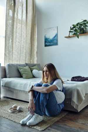 A teenage girl sits comfortably on the floor, reflecting in her stylish room filled with decor.の写真素材