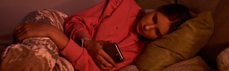 A teenage girl relaxes in her modern room, scrolling through her phone in soft evening light, bannerの写真素材