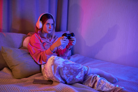 A teenage girl enjoys a fun gaming evening, immersed in her vibrant room's light.の写真素材