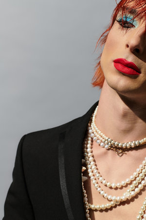 A young man showcases vibrant makeup and layered pearl necklaces against a gray backdrop.の写真素材