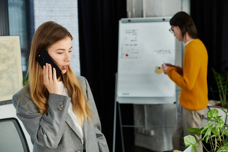 A young person in a stylish outfit talks on the phone while someone works nearby.