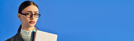 Young woman expresses emotions while holding a notebook, posing against a striking blue backdrop.の写真素材