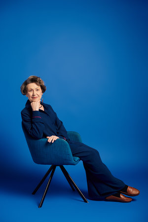 A beautiful woman in her 60s sits gracefully in chic attire, radiating confidence and charm.の写真素材