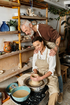 Mature couple focuses on shaping clay in a pottery class, sharing joy and creativity.の写真素材