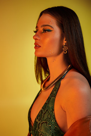 A young woman poses elegantly, showcasing her bold makeup and trendy snake-print outfit.