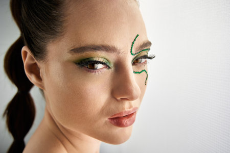 A beautiful young woman poses confidently with captivating snake makeup in a creative studio.