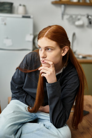 A young man with long hair ponders while sitting comfortably in his stylish apartment.