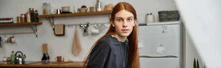A good looking young man with long hair casually relaxes in his contemporary apartment, banner