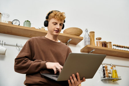 A handsome young man with red hair focused on his laptop in a stylish kitchen space.