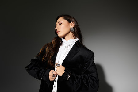 A stylish young woman with shiny brown hair poses gracefully against a grey backdrop.