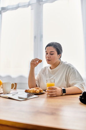 Savoring a morning meal, a young plus sized woman enjoys pastries and juice at a rustic table.