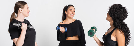 Three fit women share a fun workout session, smiling and lifting weights in stylish sportswear.の写真素材