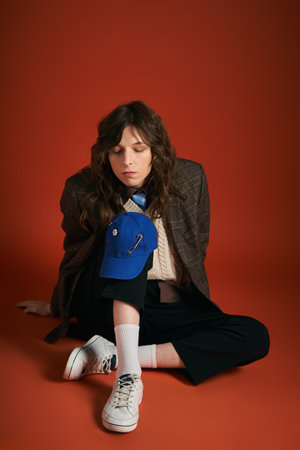 A stylish young man sits on the floor, deep in thought in a trendy outfit.のeditorial素材