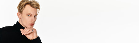 A young handsome man poses thoughtfully against a simple white backdrop, showcasing elegance.の写真素材