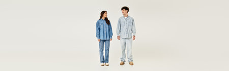 A fashionable couple stands closely, wearing modern denim outfits in a bright, neutral space.の写真素材