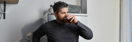 A man with a charming demeanor sips a beverage while leaning against the kitchen counter.