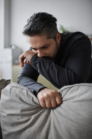 A thoughtful man leans on a sofa, deep in contemplation, surrounded by a calm and cozy environment.