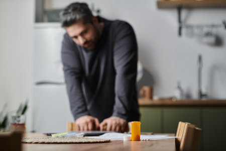 A handsome man leans forward thoughtfully at a table in a warm kitchen.の写真素材