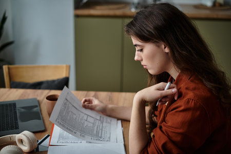 A woman sits at a table, absorbed in her paperwork, reflecting feelings of sadness and anxiety.のeditorial素材