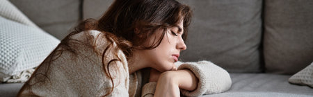 A woman sits alone on a soft sofa, her expression reflecting deep sadness and contemplation.