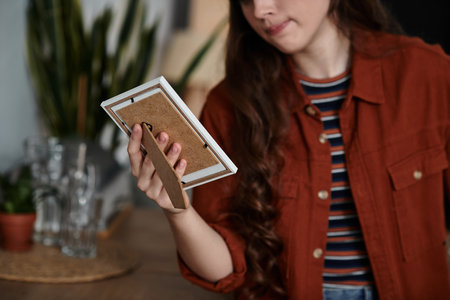 In a calm indoor space, a woman holds a framed picture, deep in thought.