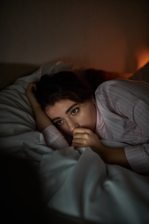 A woman lays curled up on her bed, displaying the weight of her troubled thoughts in a soft glow.