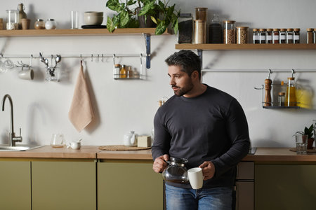 A handsome man pours coffee in his stylish kitchen, surrounded by greenery.のeditorial素材
