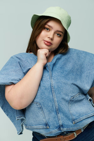 Confident plus size woman models stylish denim and a trendy hat with a delightful smile.のeditorial素材