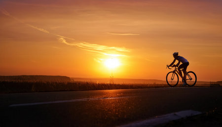 Bicyclist enjoys a vibrant summer sunset on a peaceful rural road.の素材