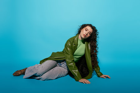 A young woman in a green leather jacket lounges gracefully on the floor, exuding confidence.のeditorial素材