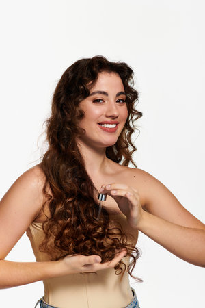 A stylish young woman smiles while showcasing a hair care product in bright light.のeditorial素材