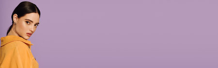 A beautiful young woman with dark hair showcases her trendy fashion sense in a soft lilac setting.