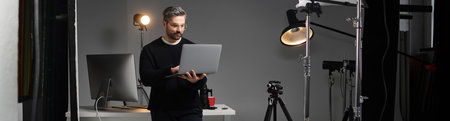 A man focuses on his laptop while surrounded by photography equipment in a modern workspace.