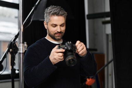 A focused person adjusts camera settings, readying for a shoot in the dim studio light.のeditorial素材