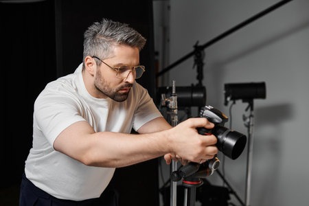 Focused individual adjusts camera equipment while preparing for a creative photo shoot indoors.の写真素材