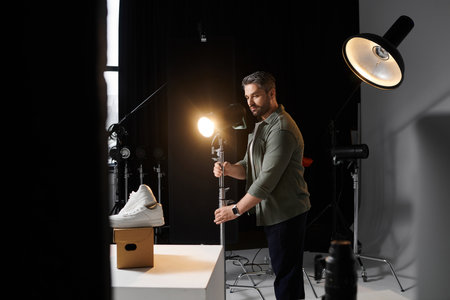 A man skillfully arranges the lighting for an attractive sneaker display in a photography studio.のeditorial素材