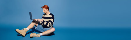 A young, handsome man sits on the floor, absorbed in his laptop in a bright room.のeditorial素材