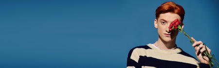 A handsome young man with red hair expresses feelings while holding a rose close to his face.のeditorial素材