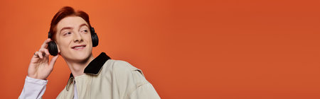 A young and handsome man listens to music with a smile, radiating emotion in a bold orange backdrop.のeditorial素材