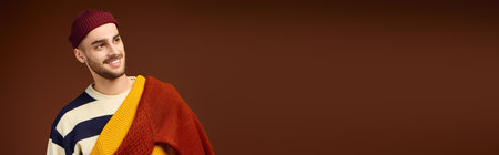 Stylish young man wears a fashionable outfit and beanie against a modern brown background, banner