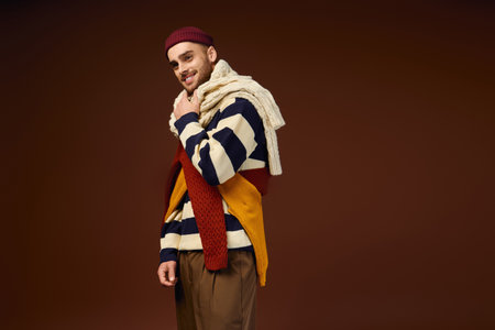 A young man models a trendy outfit featuring a stylish beanie and layered winter knits.