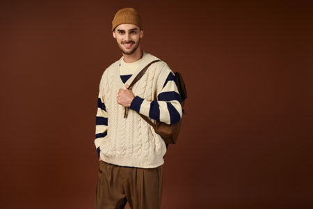 A happy young man in a beanie poses confidently against a warm backdrop.