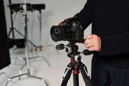 A focused man adjusts his camera on a tripod, preparing for an indoor photoshoot in the studio.